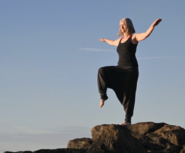 Die Qigong-Bewegung "Der Goldene Hand steht auf einem Bein" vor Himmel. Einbeinige Position mit seitliche geöffneten Armen.
